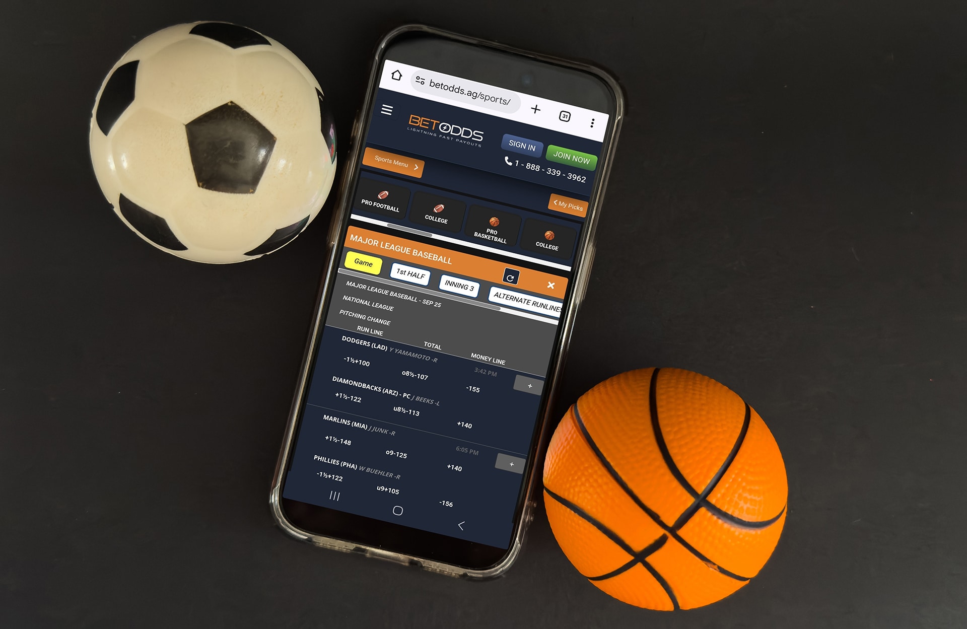 A photo of a mobile device displaying a page from the BetOdds website on a black background. There is a soccer ball and a basketball on either side of the phone.