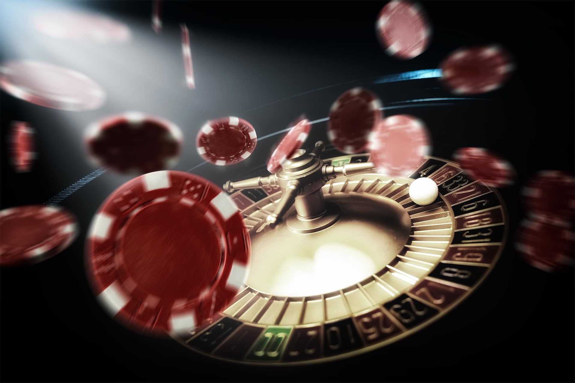 Casino roulette wheel with a white ball spinning and red poker chips flying through the air under dramatic lighting.