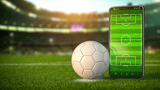 A photo of a soccer ball on a field and next to it a mobile phone showing the same field on the screen.